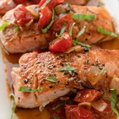 two pieces of salmon with tomatoes and onions on a white plate