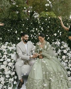 a man and woman sitting on a bench surrounded by flowers with petals flying around them