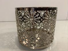 a silver vase with intricate designs on it sitting on a white counter top next to a wall