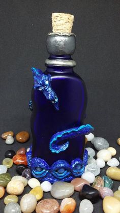 a blue glass bottle with a dragon on it surrounded by rocks and stones, next to a corkscrew