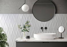 a white sink sitting under a round mirror next to a potted plant on top of a counter