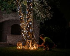 a person sitting on the ground in front of a tree with some lights around it