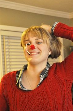 a woman with a clown nose and red nose ring smiles at the camera while wearing a sweater