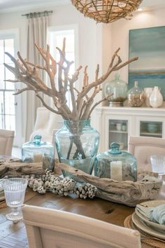 a dining room table is decorated with blue glass vases and driftwood branches for centerpieces