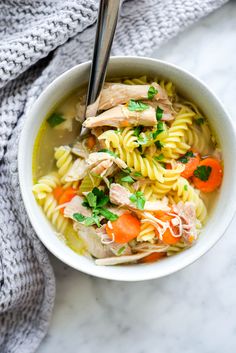 a white bowl filled with chicken noodle soup on top of a table next to a gray towel