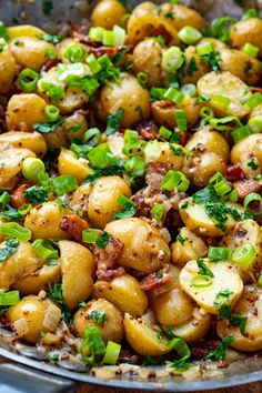 a pan filled with potatoes covered in bacon and chopped green onions on top of a wooden table