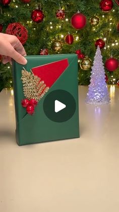 someone is opening up a christmas present in front of a tree with red and green decorations