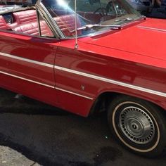 an old red convertible car parked in a parking lot