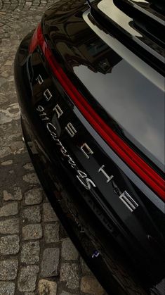 the back end of a black porsche car parked on a cobblestone street in front of a building