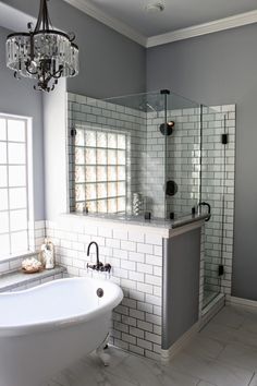 a white tub sitting next to a shower in a bathroom under a chandelier