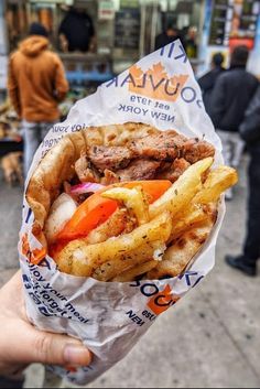 a person holding up a sandwich and french fries on the street in front of people