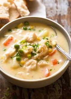 a bowl of chicken and dumpling soup on a wooden table with bread in the background