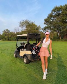 a woman standing next to a golf cart on top of a green grass covered field