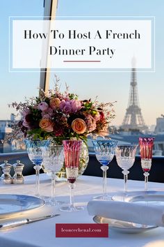 a table with wine glasses and flowers on it in front of the eiffel tower