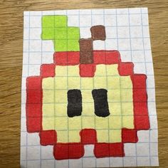 an apple made out of colored squares sitting on top of a wooden table next to a piece of paper