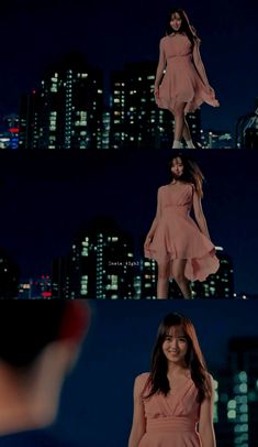 a woman in a pink dress standing on top of a building at night with city lights behind her