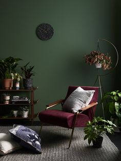 a living room with green walls, plants and a chair in front of a clock