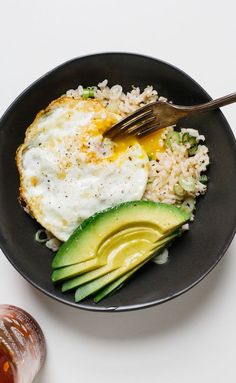 an egg and avocado on top of rice in a black bowl with a fork