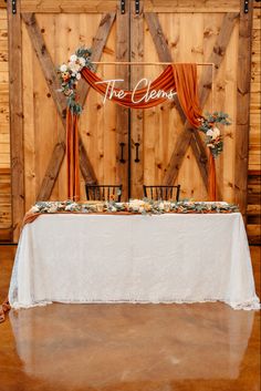 the table is set up with an orange drape and floral centerpieces on it