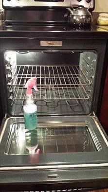 an open oven with a bottle of cleaner on the top and bottom, in front of it