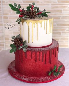 a red and white christmas cake with gold drips, holly leaves and pine cones