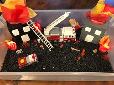 a plastic container filled with black gravel and firetrucks on top of it