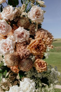 an arrangement of flowers in a vase sitting on a table with the sky in the background