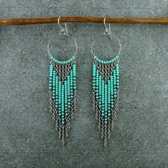 two pairs of turquoise and black seed beaded earrings on a wooden stick next to a gray surface