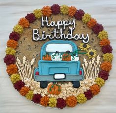 a birthday cake with a blue truck and pumpkins on the front, surrounded by flowers