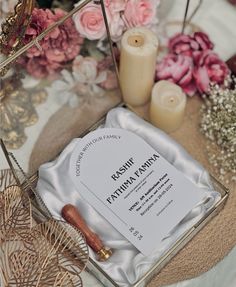 a close up of a paper on a table with candles and flowers in the background