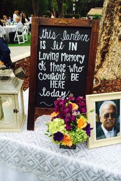 a table with flowers and pictures on it, next to a sign that says this lantern is lit in loving memory so those who could be here today