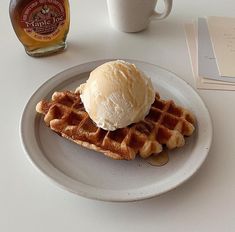 a plate with waffles and ice cream on it next to a bottle of maple syrup