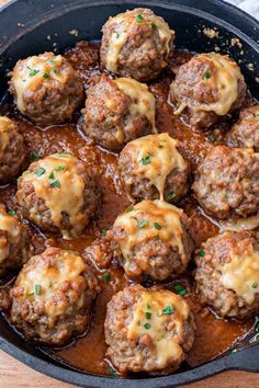 a skillet filled with meatballs covered in gravy and sauce on top of a wooden table