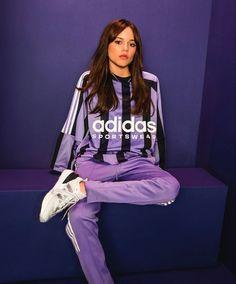 a woman sitting on top of a blue bench wearing purple sweatpants and adidas sneakers