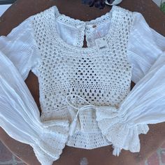 a white top with crochet detailing on the shoulders and sleeves, sitting on a table