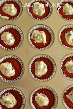 twelve cupcakes with white icing sitting on top of a cookie sheet in muffin tins