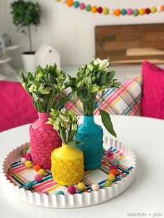 three vases with flowers in them are sitting on a tray that is decorated with pom poms