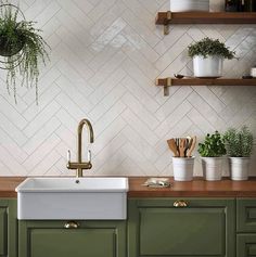 a kitchen with green cabinets and white tiled backsplash, brass faucet