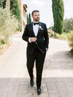 a man in a tuxedo is walking down the street with his hand in his pocket