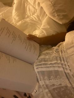 an open book laying on top of a bed next to a woman's hand