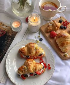 two croissants on a plate with berries and strawberries next to a cup of tea