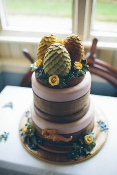 a three tiered cake decorated with pine cones and flowers