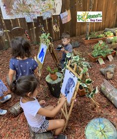 three children are painting pictures in the yard with their easels and potted plants