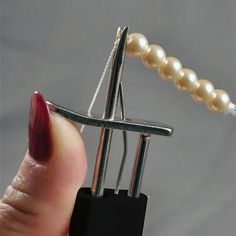 a person is holding a tiny metal object with pearls on it's end and the tip of their finger