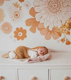 a baby sleeping on top of a white dresser next to a flower wallpapered wall