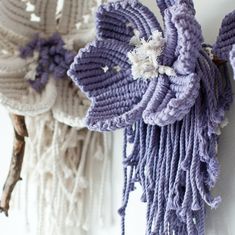 two purple and white crocheted flowers hanging from hooks on a wall next to each other