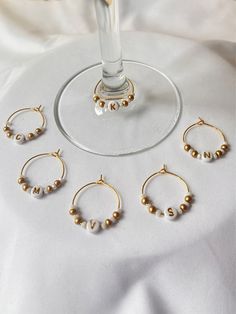 the wine glass is next to five pairs of gold beaded hoop earrings on a white tablecloth