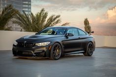 a black bmw car parked in front of a tall building with palm trees behind it