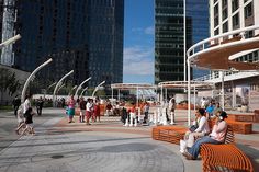 people are sitting on benches in the city square with tall buildings and skyscrapers behind them