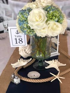 a vase with flowers and seashells sits on a table at a wedding reception